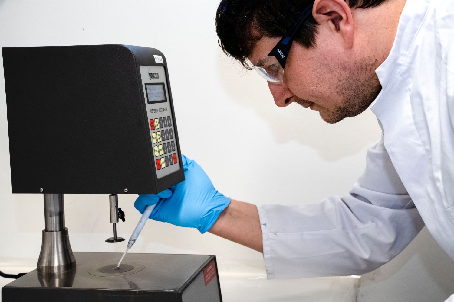 A man in a white coat dispenses something from a pipette onto a surface