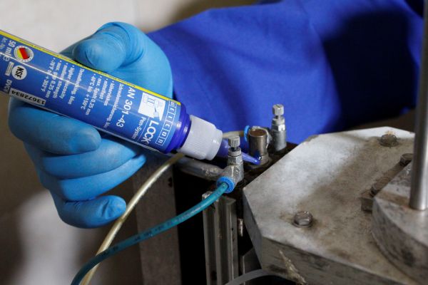 A person wearing a blue glove applies WEICONLOCK AN 301-43 threadlocker onto a metal screw on an industrial component.